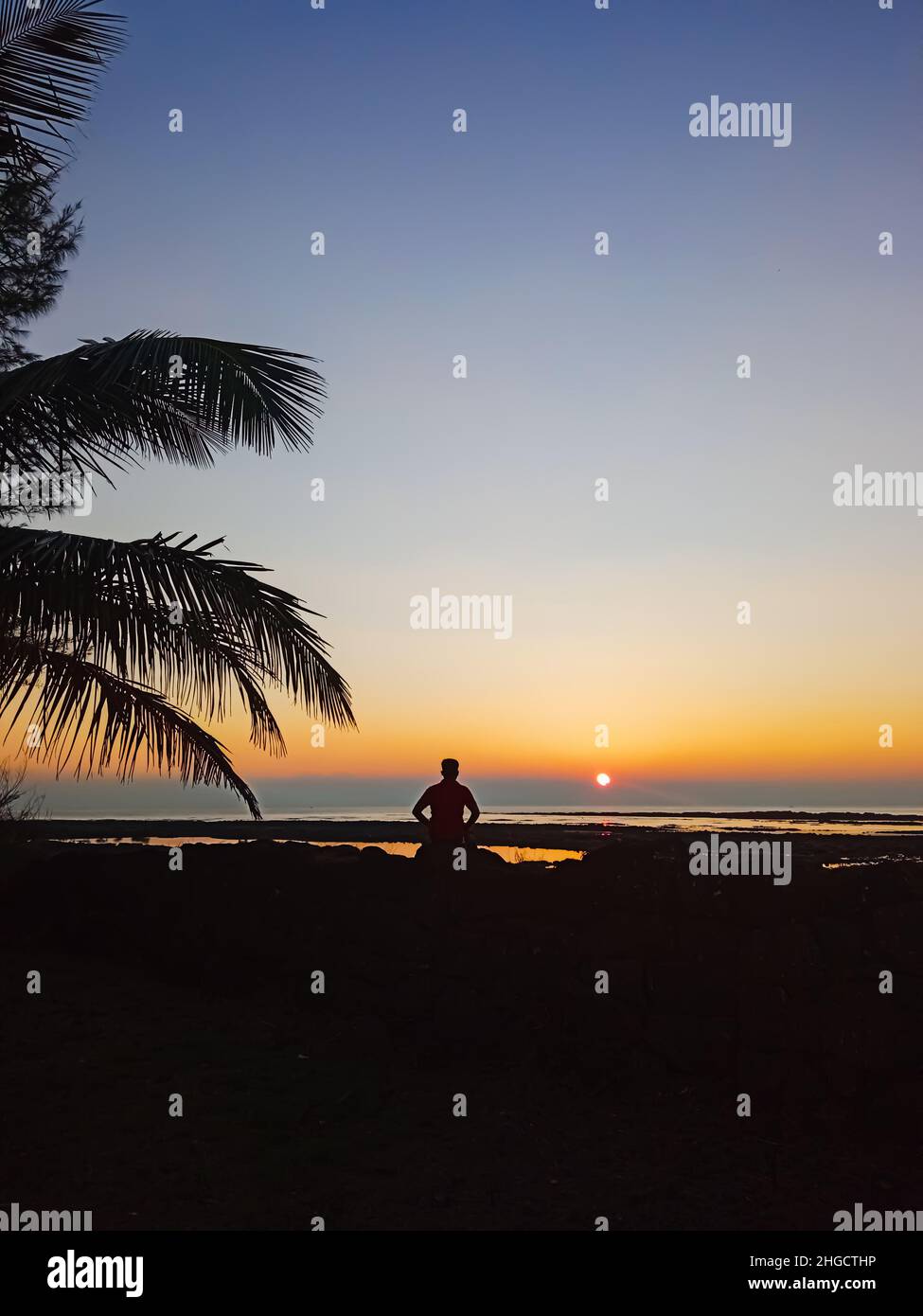 Incredibile tramonto sulla spiaggia e solo uomo seduto sulla pietra Foto Stock
