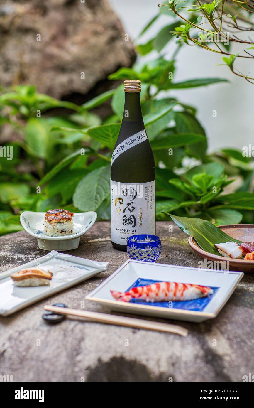 Sushi set e sashimi con sake serviti su pietra grigia con giardino sullo sfondo. Foto Stock