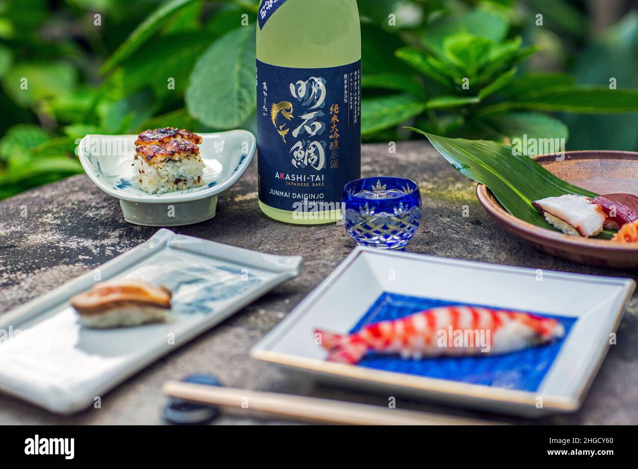 Sushi set e sashimi con sake serviti su pietra grigia con giardino sullo sfondo. Foto Stock