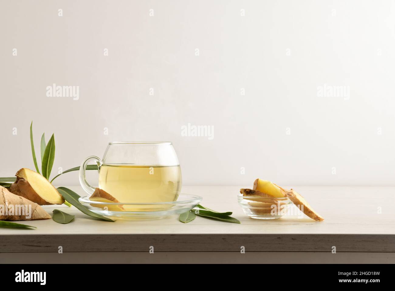 Tazza per bevande allo zenzero caldo su un tavolo di legno con radice di zenzero e foglie di fondo bianco isolato. Vista frontale. Foto Stock