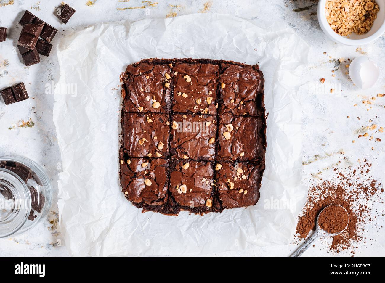 Brownie al cioccolato fondente con briciole di nocciola sulla parte superiore, su un vassoio con polvere di cacao, briciole di cioccolato su un fondo bianco rustico. Foto Stock