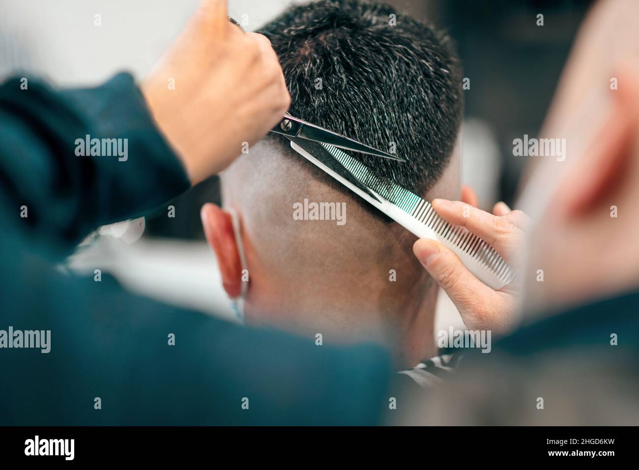 Barbiere professionista con forbici e pettine per tagliare i capelli di un uomo in un moderno acconciatura a forma di V in una vista posteriore ravvicinata sulle mani e sul to Foto Stock