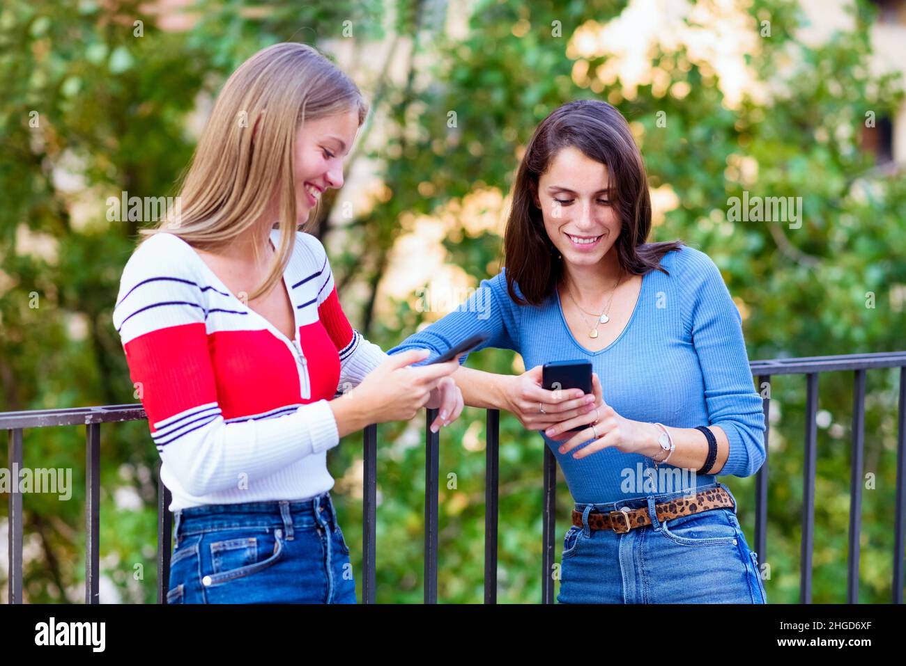 Due belle giovani donne e i migliori amici sorridono mentre usano i loro telefoni cellulari per divertimento e social media all'aperto Foto Stock