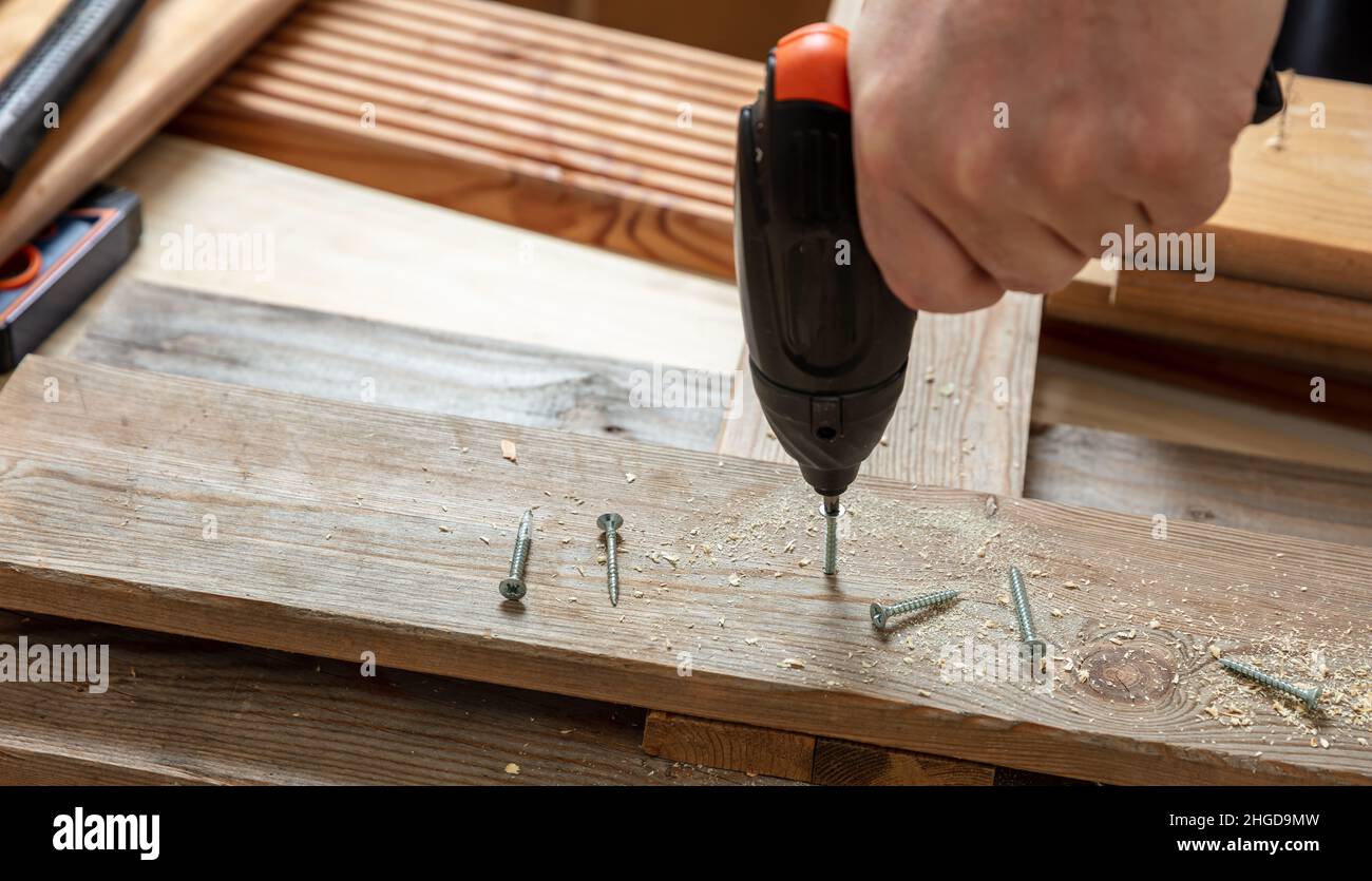 Cacciavite elettrico, vite a mano maschio su legno. Tavolo da lavoro da carpentiere con vista a primo piano. Fai da te, riparazione e riparazione in casa. Foto Stock