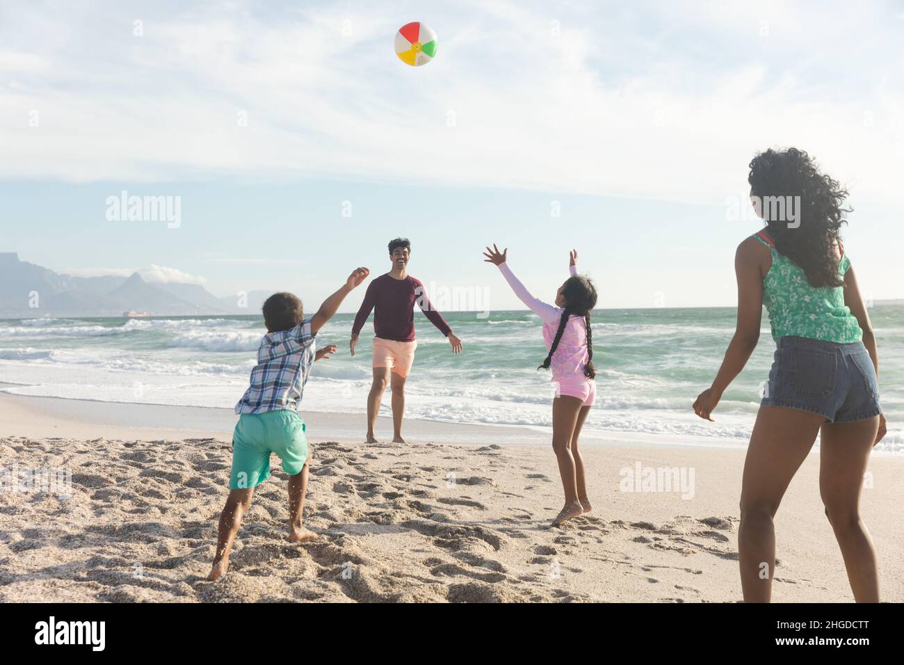 Felice famiglia multirazziale giocare con palla sulla sabbia in spiaggia contro il cielo durante la giornata di sole Foto Stock