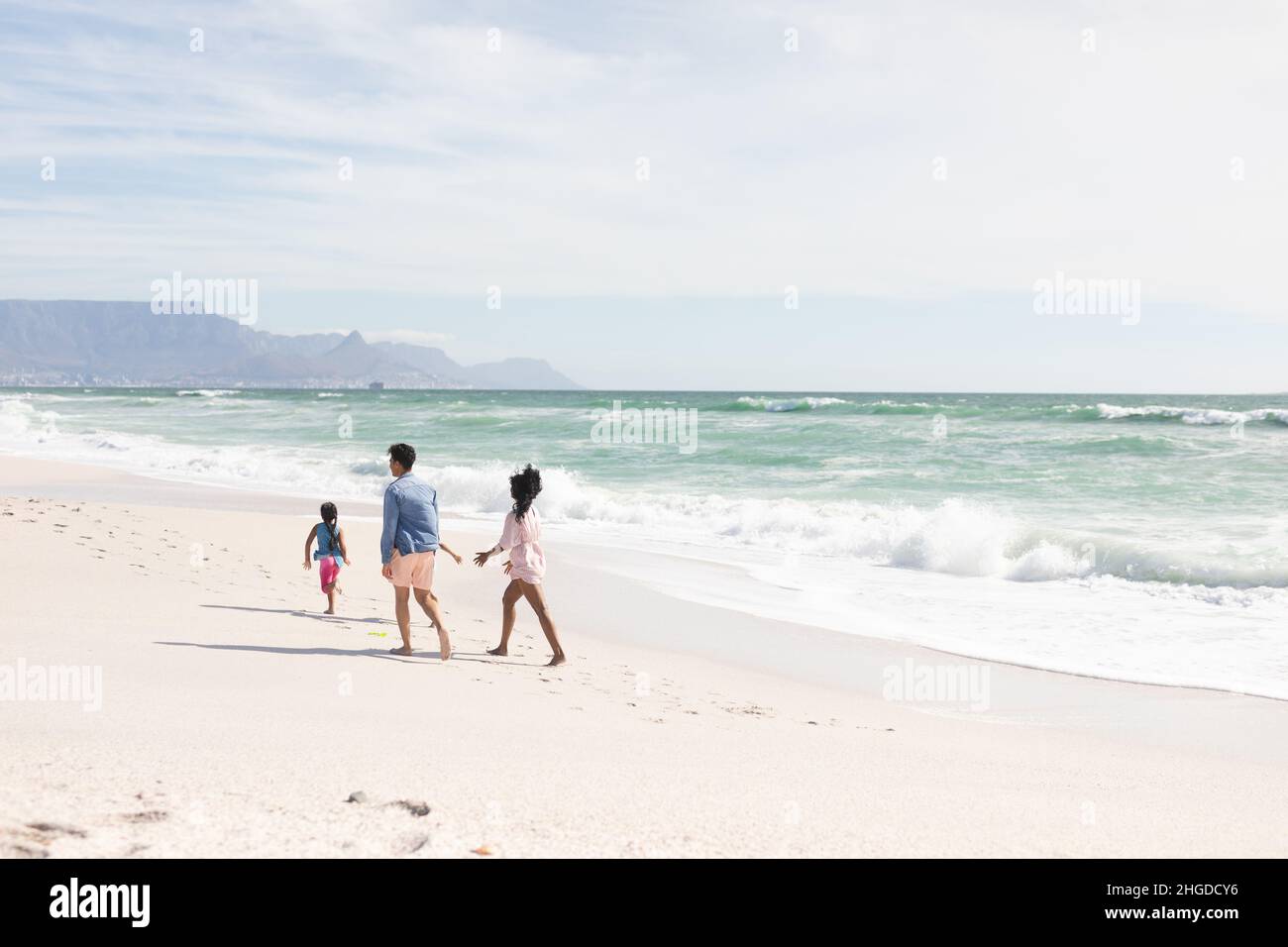 Tutta la lunghezza dei genitori multirazziali che camminano dietro il figlio sulla riva alla spiaggia durante la giornata di sole Foto Stock
