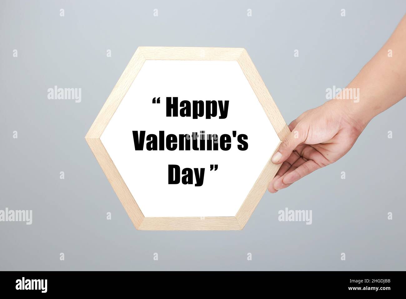 Le mani da uomo con cornice esagonale hanno scritto il giorno di San Valentino in uno stile femminile minimalista, morbido sfondo di lino grigio - perfetto per San Valentino D. Foto Stock