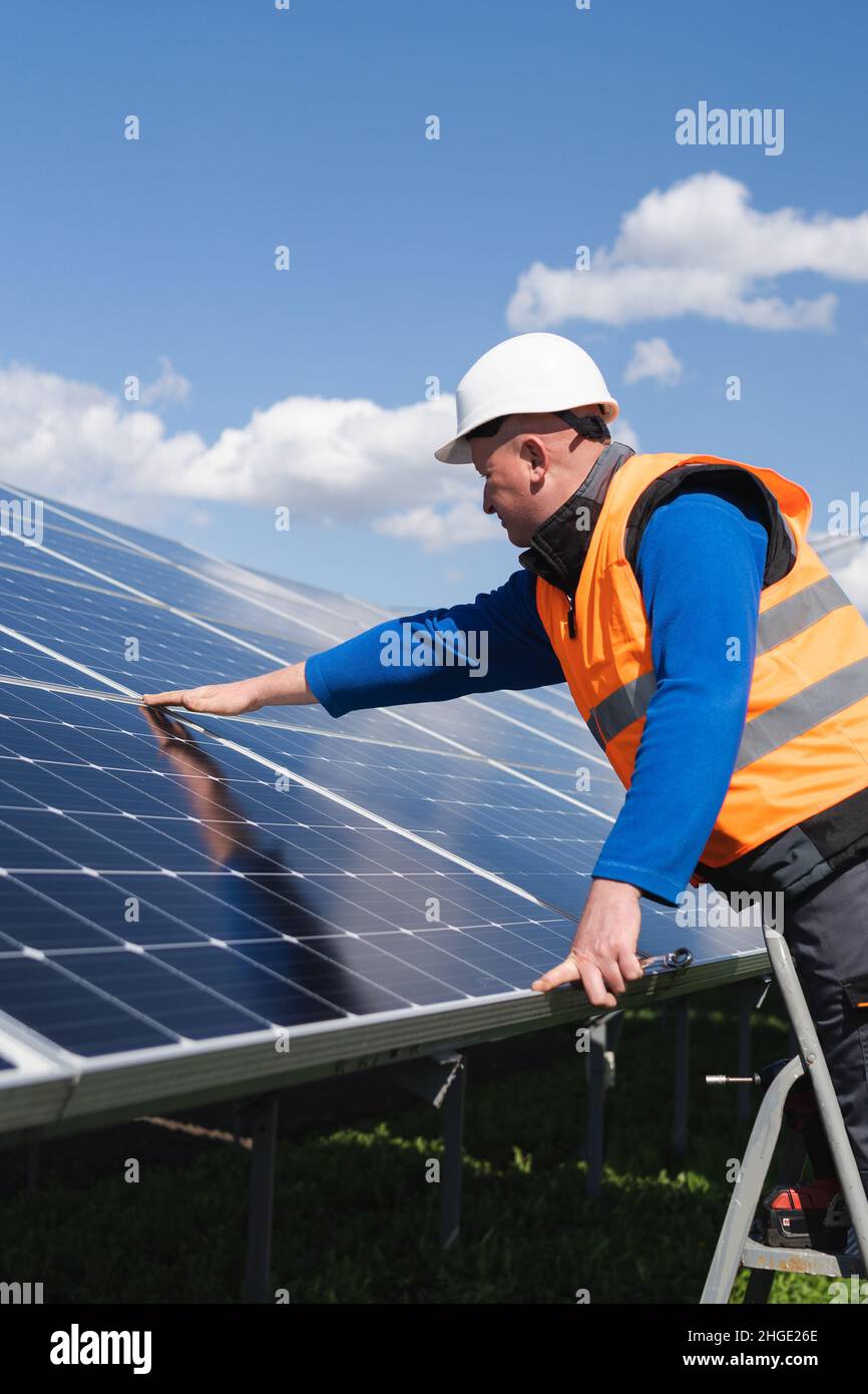 Il lavoratore di pianta di energia solare sulla scala a cavalletto fa un'ispezione visiva dei pannelli solari Foto Stock