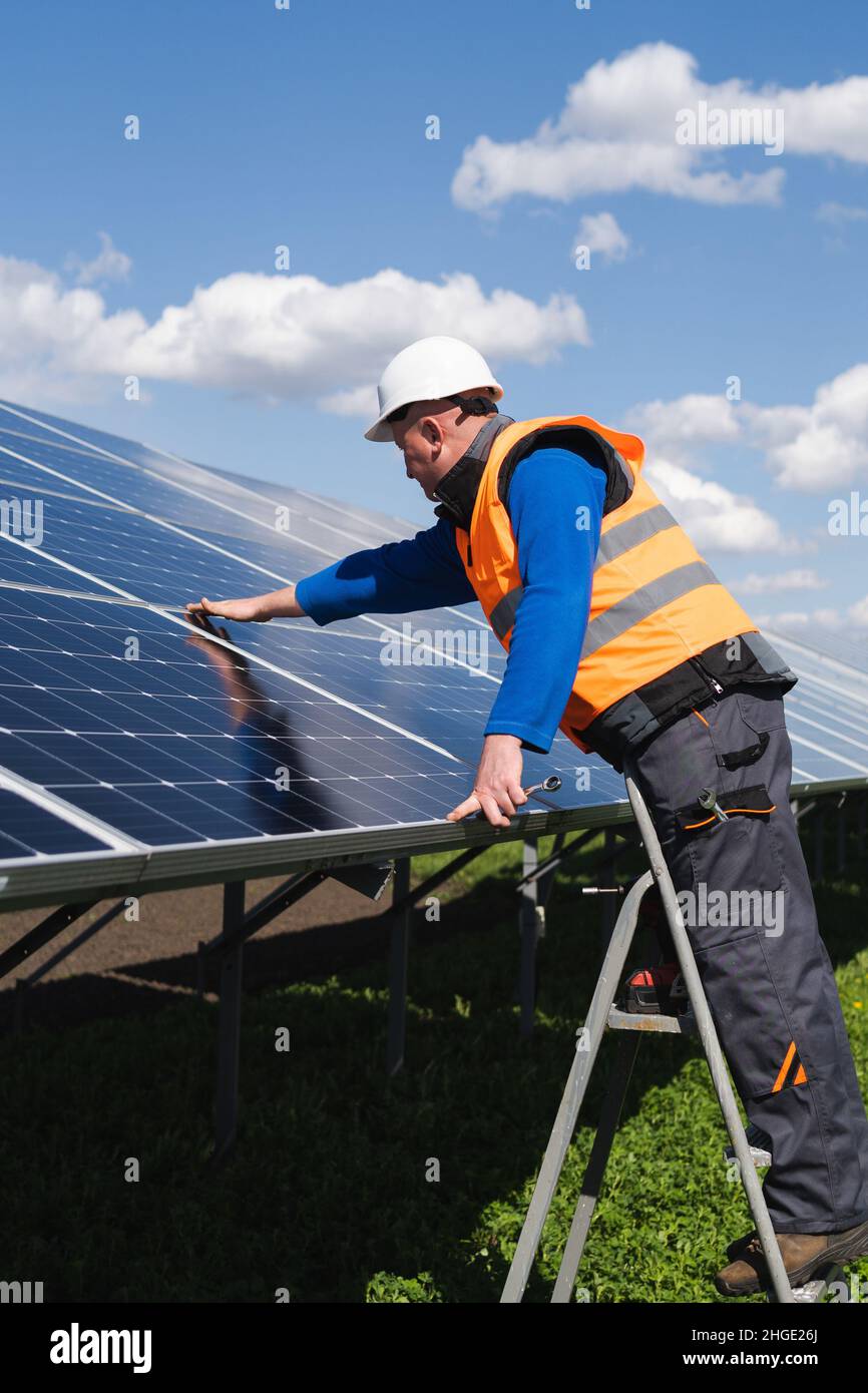 Il lavoratore di pianta di energia solare sulla scala a cavalletto fa un'ispezione visiva dei pannelli solari Foto Stock