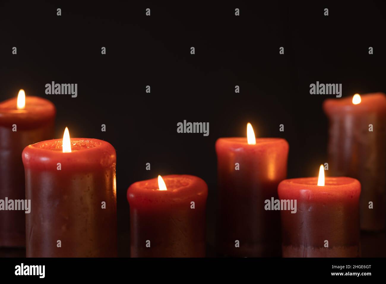 Candele rosse illuminate in una stanza buia con uno sfondo nero con spazio copia Foto Stock