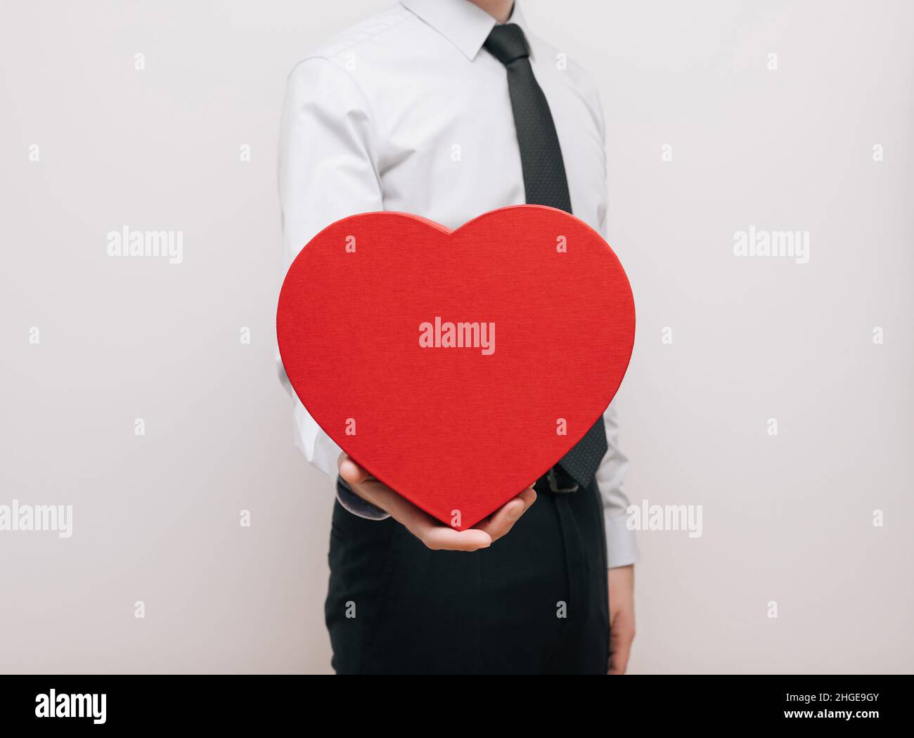 Uomo con grande cuore rosso dono in mano su sfondo bianco. Concetto di giorno dell'amore e di San Valentino. Spazio di copia. Foto Stock