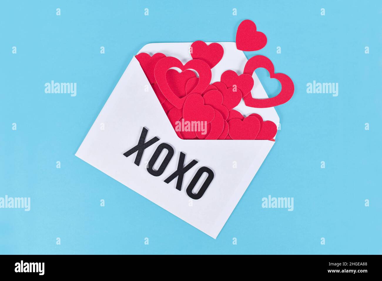 Lettera d'amore bianca con cuori che fuoriescono e lettere XOXO su sfondo blu Foto Stock