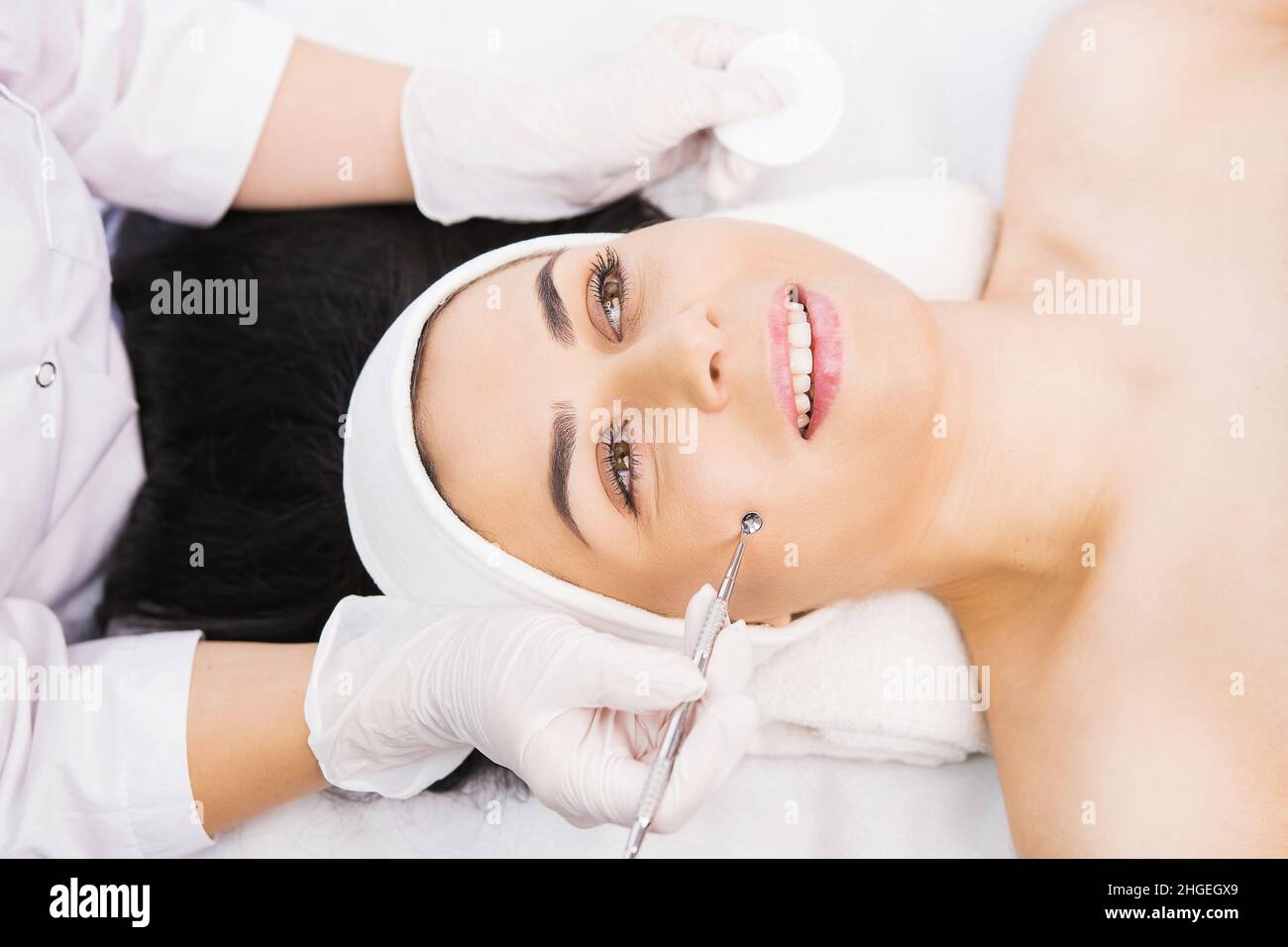 Il cosmetologo professionista esegue la procedura dermapen nella clinica di cosmetologia ad una donna, cosmetica del viso, pulizia manuale meccanica del viso con uno Foto Stock