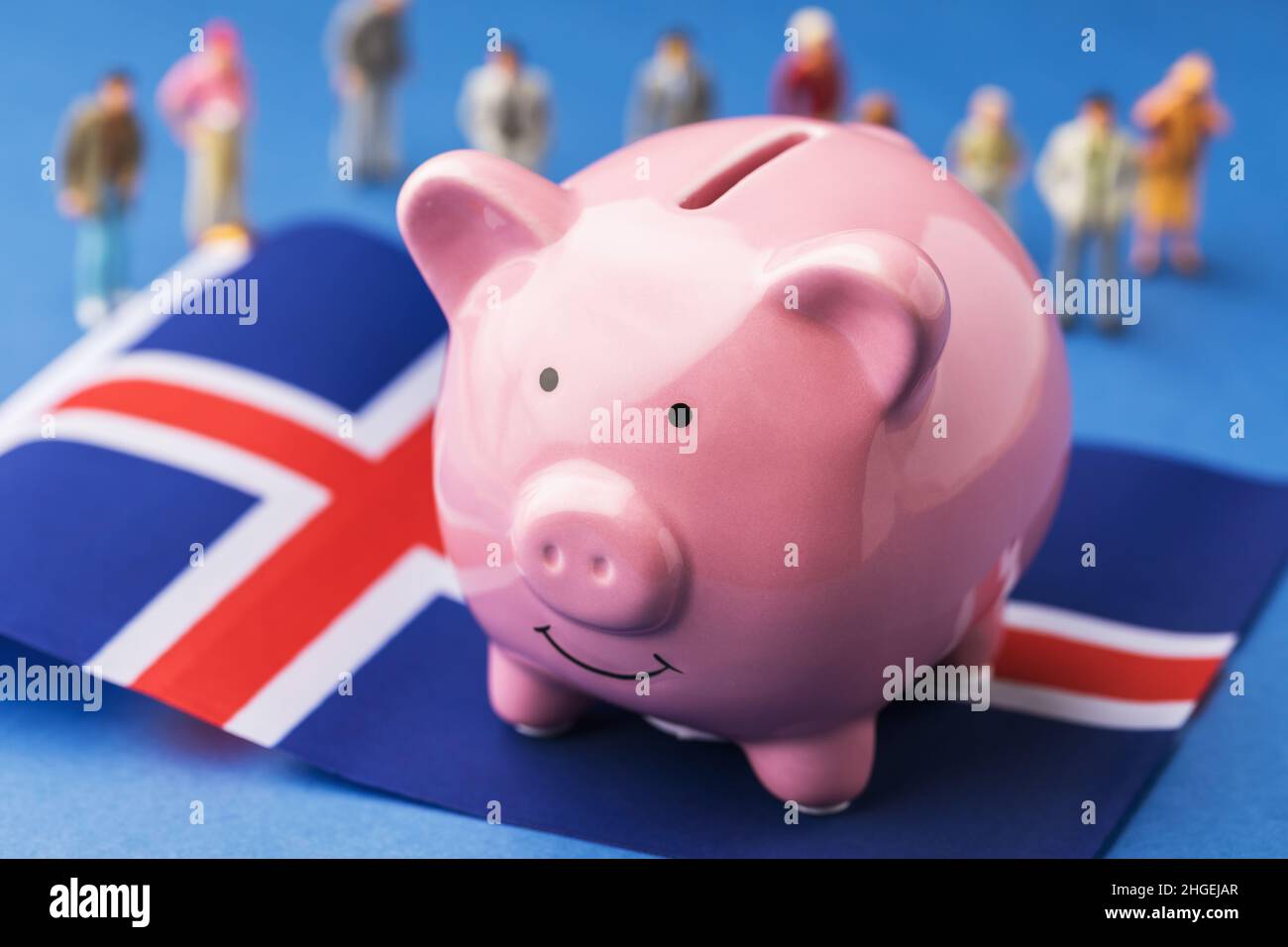 Piggy banca, bandiera islandese e giocattoli di plastica uomini su uno sfondo colorato, il concetto sul tema del reddito della popolazione islandese Foto Stock