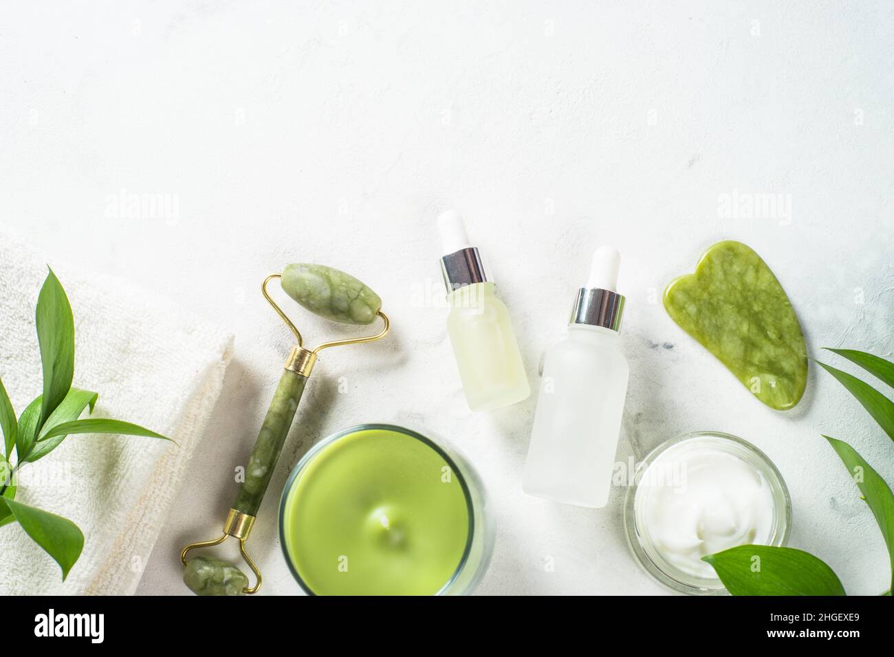 Massaggiatore Jade Roller e pietra gua sha con crema per il viso e bottiglia di siero. Foto Stock
