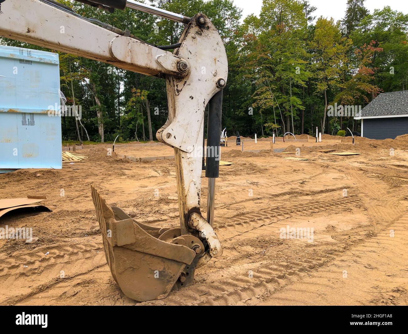 L'attrezzatura pala a cucchiaio retroescavatore, utilizzata sull'escavatore per la movimentazione del terreno o della ghiaia, poggia sullo sporco in un cantiere di costruzione di una casa, vicino a un cumulo di blu Foto Stock