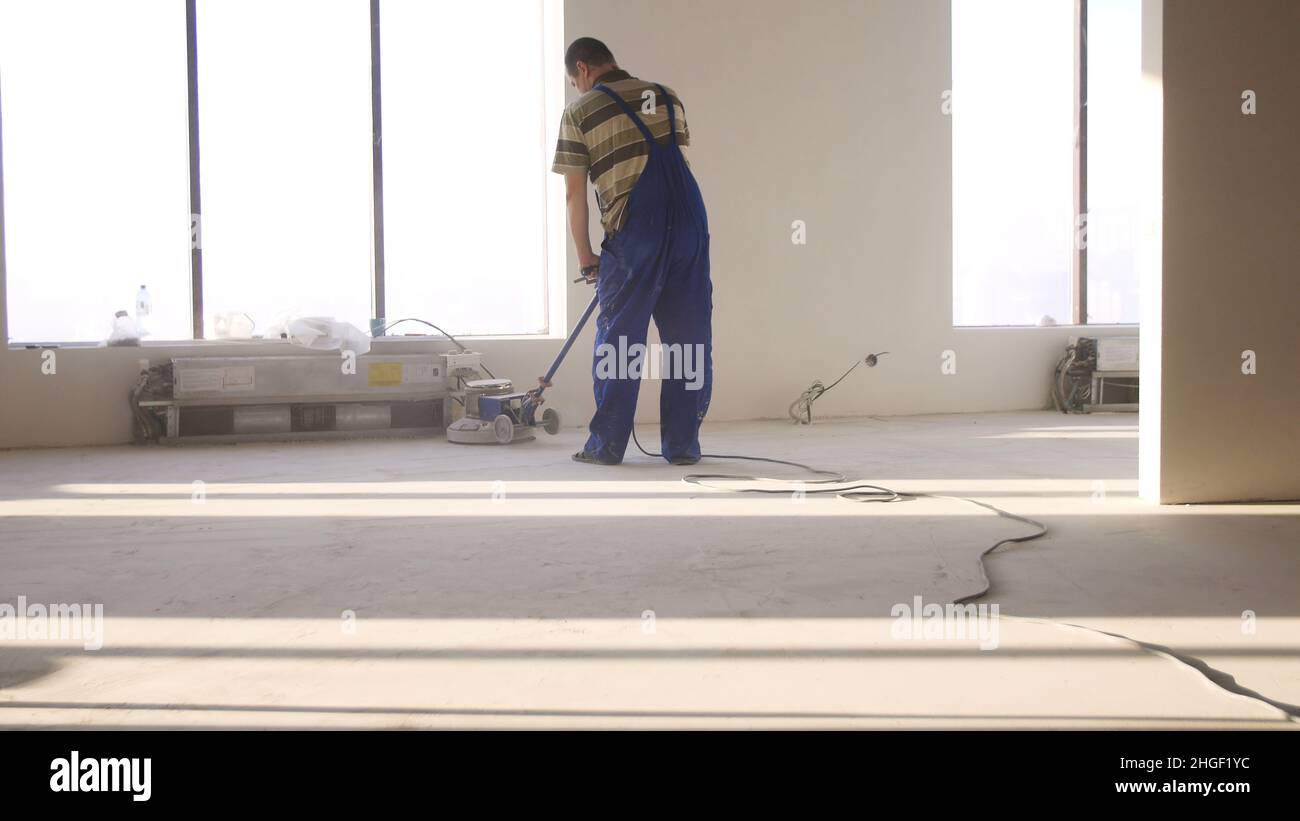 Lavori di ristrutturazione, levigatura parquet, lucidatura. L'uomo lucida i pavimenti in camera. Riparazione di appartamenti in una casa costosa. Foto Stock