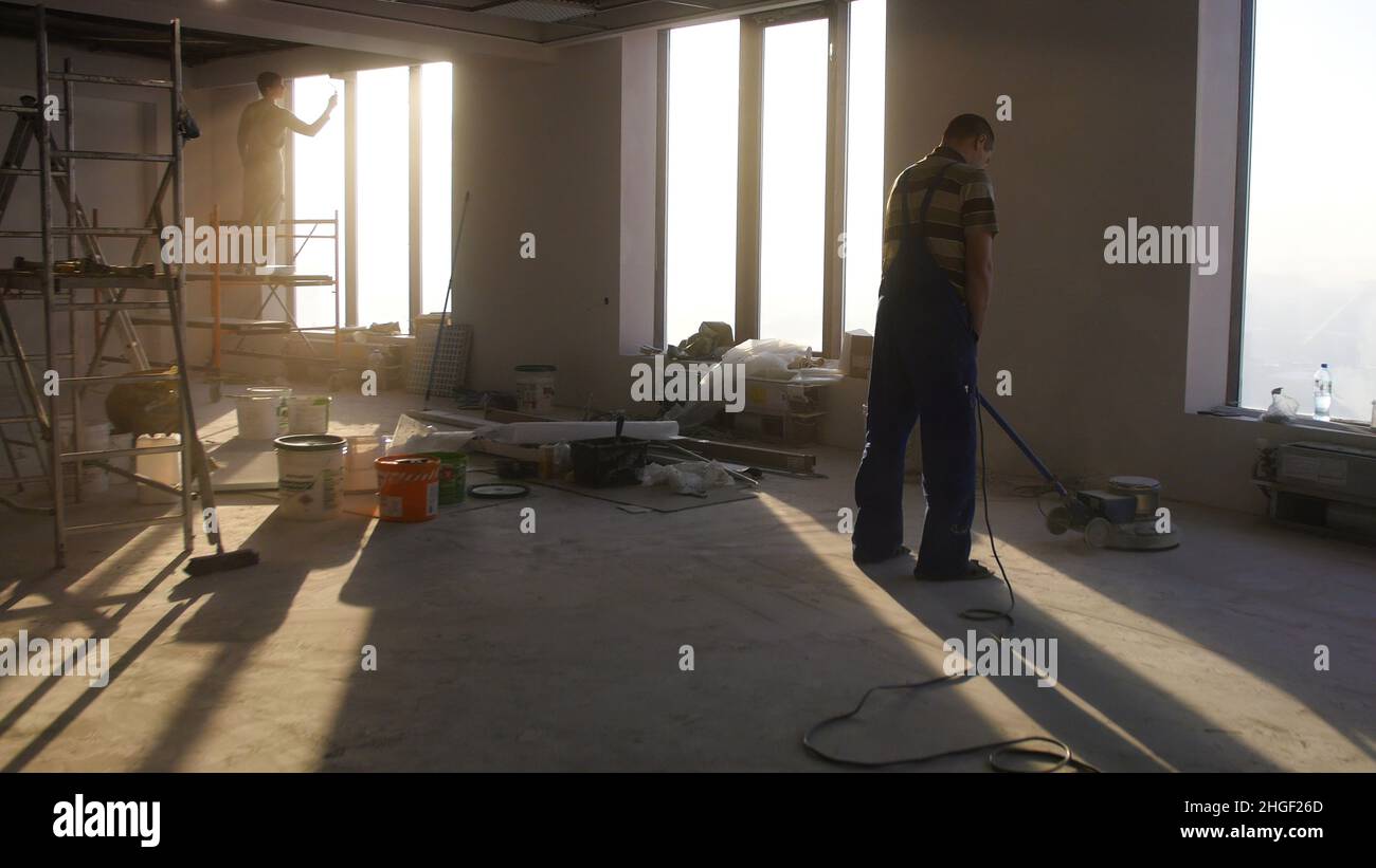 Lavori di ristrutturazione, levigatura parquet, lucidatura. L'uomo lucida i pavimenti in camera. Riparazione di appartamenti in una casa costosa. Foto Stock