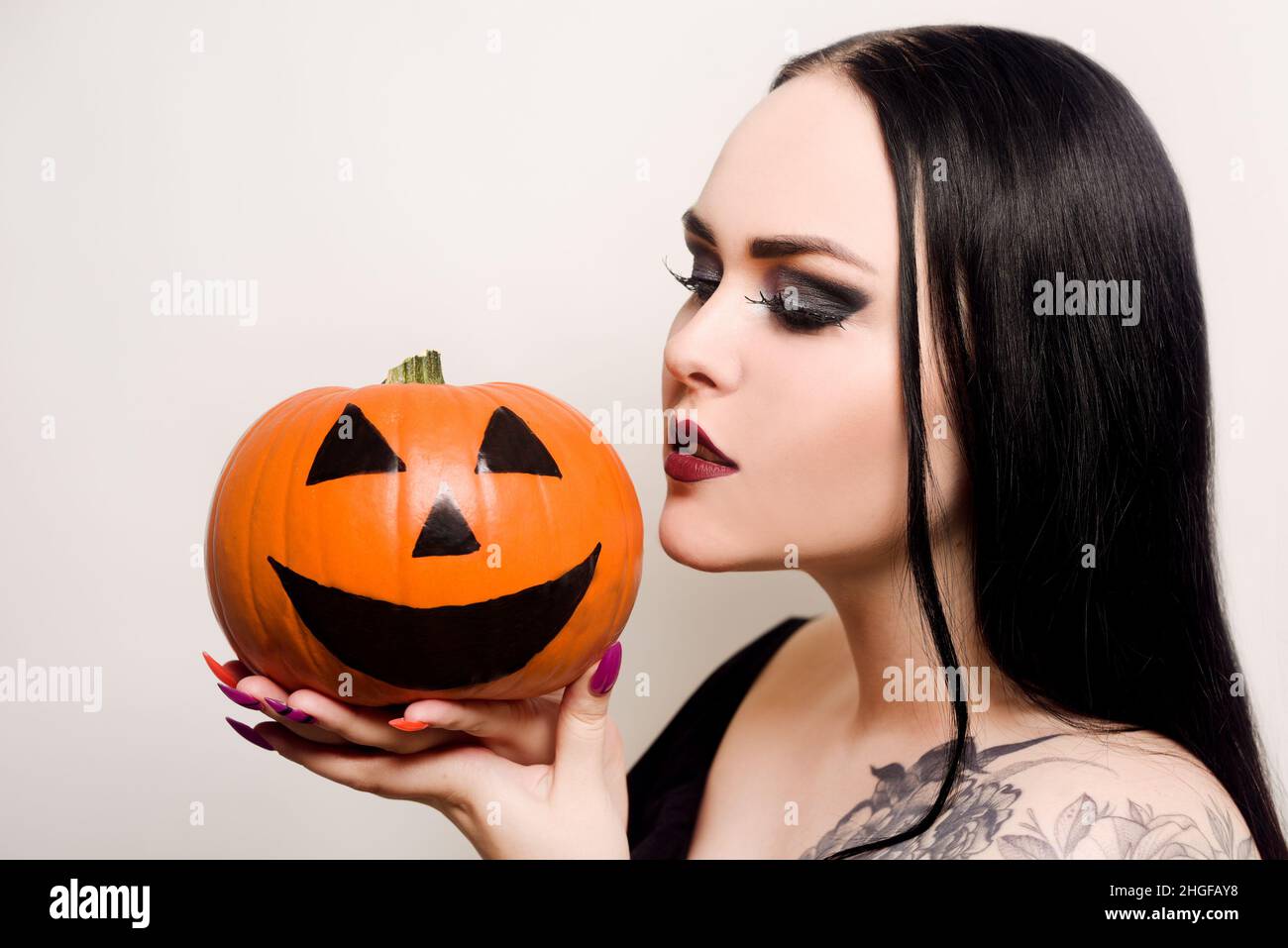 Una bella brunetta tiene una zucca nelle sue mani e la guarda. Donna con  trucco Halloween, rossetto scuro. Modello su sfondo bianco Foto stock -  Alamy