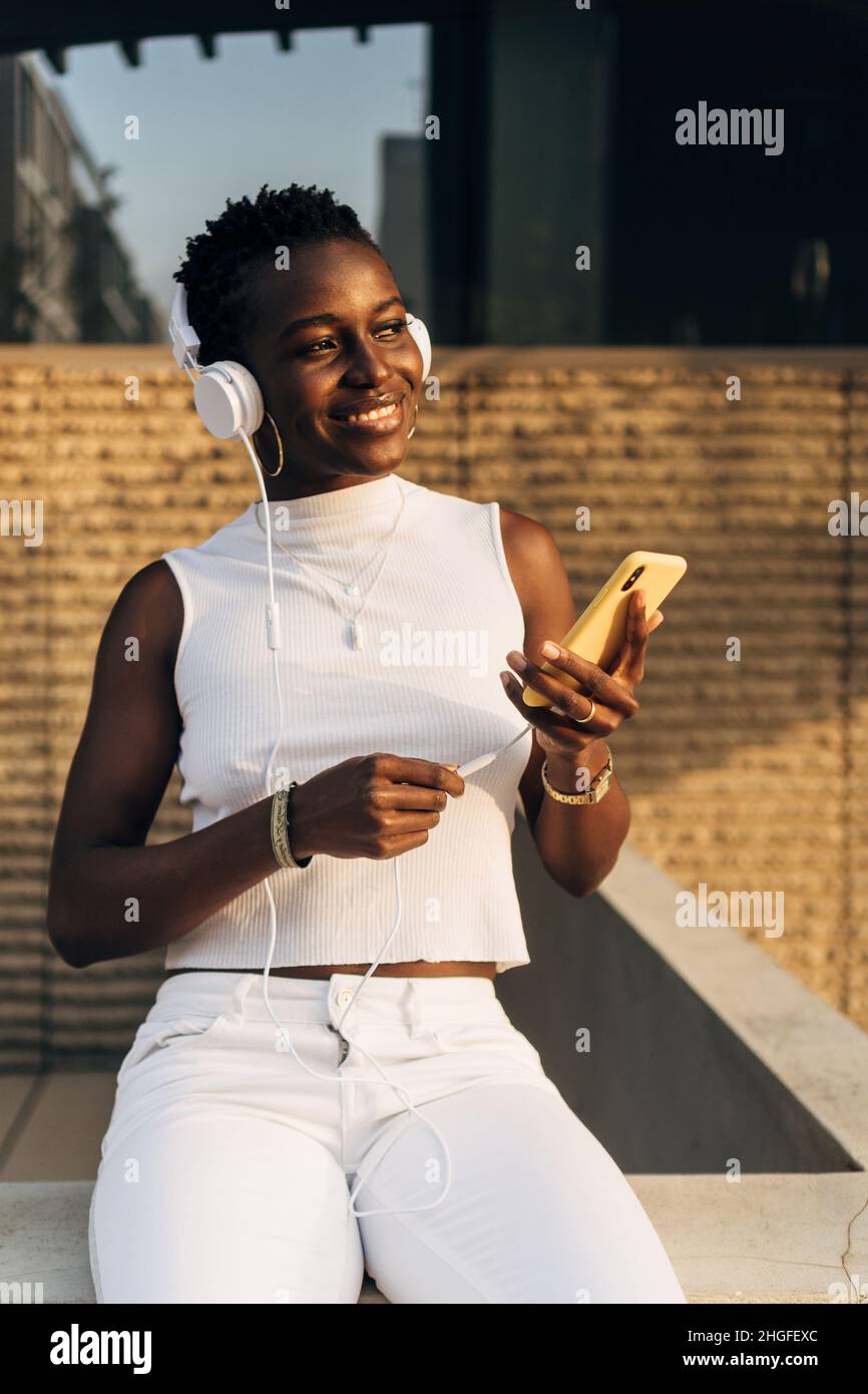 La donna afroamericana ama ascoltare la musica con un telefono cellulare e le cuffie mentre si siede all'aperto. Foto Stock