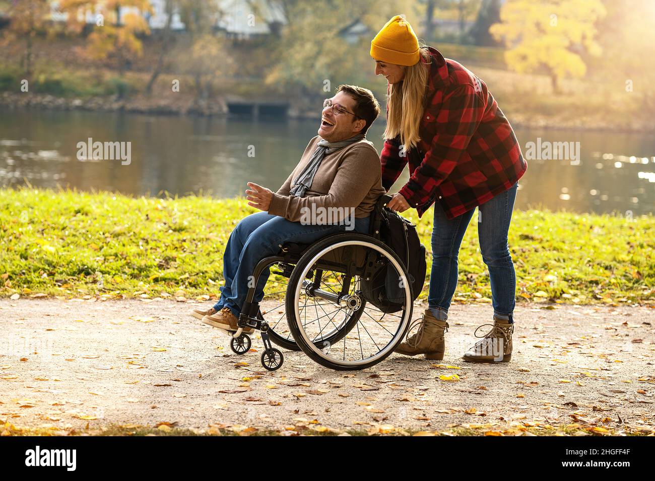 Donna e la sua amica in sedia a rotelle che hanno fatto una passeggiata attraverso il parco in un fiume godendo l'autunno Foto Stock
