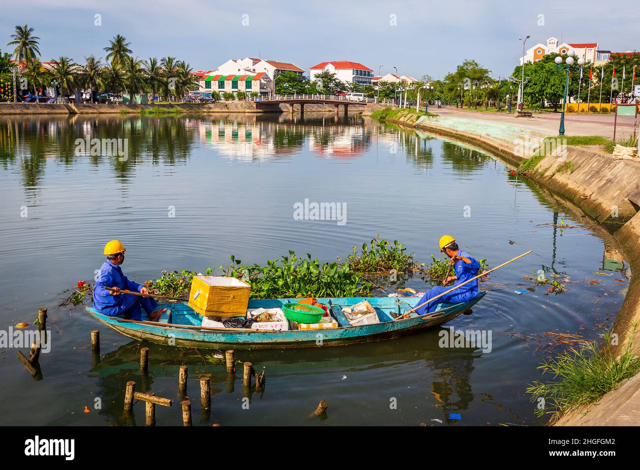 Due uomini in tute blu che puliscono l'acqua nel centro storico in una barca da 2 uomini. Foto Stock