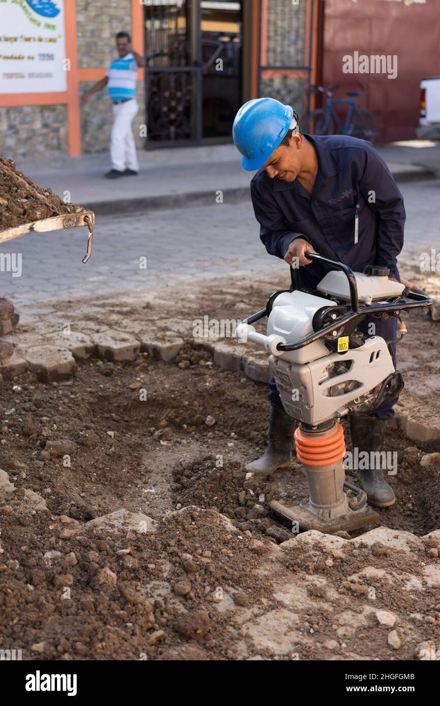 Jinotega, Nicaragua: Uomo che usa un compattatore per terreno alimentato a gas per riparare una strada dopo il wwork sulla rete idrica. Foto Stock