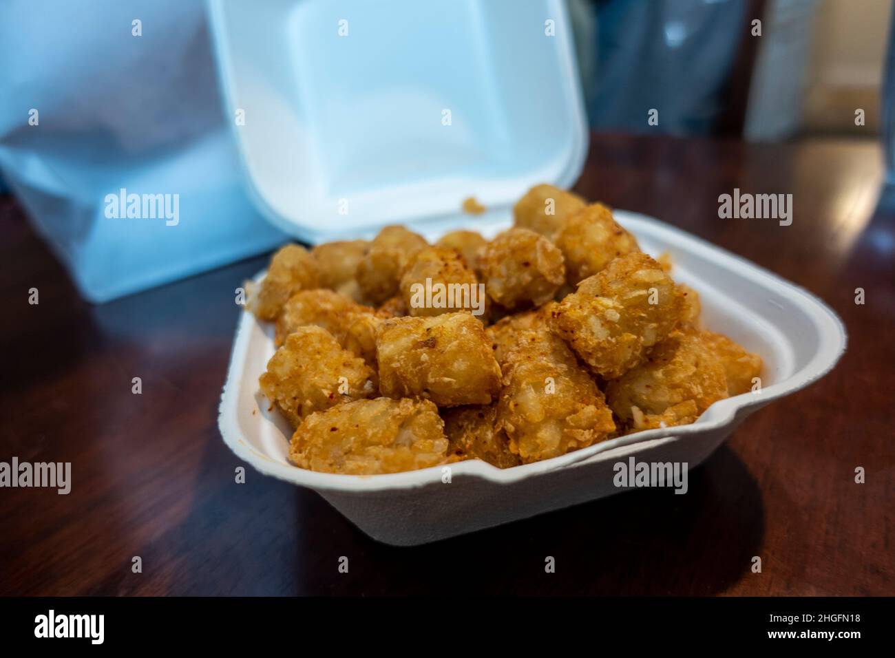 Focalizzazione selettiva di croccanti tatere marroni dorate in un contenitore bianco in polistirolo da andare da un ristorante. Foto Stock