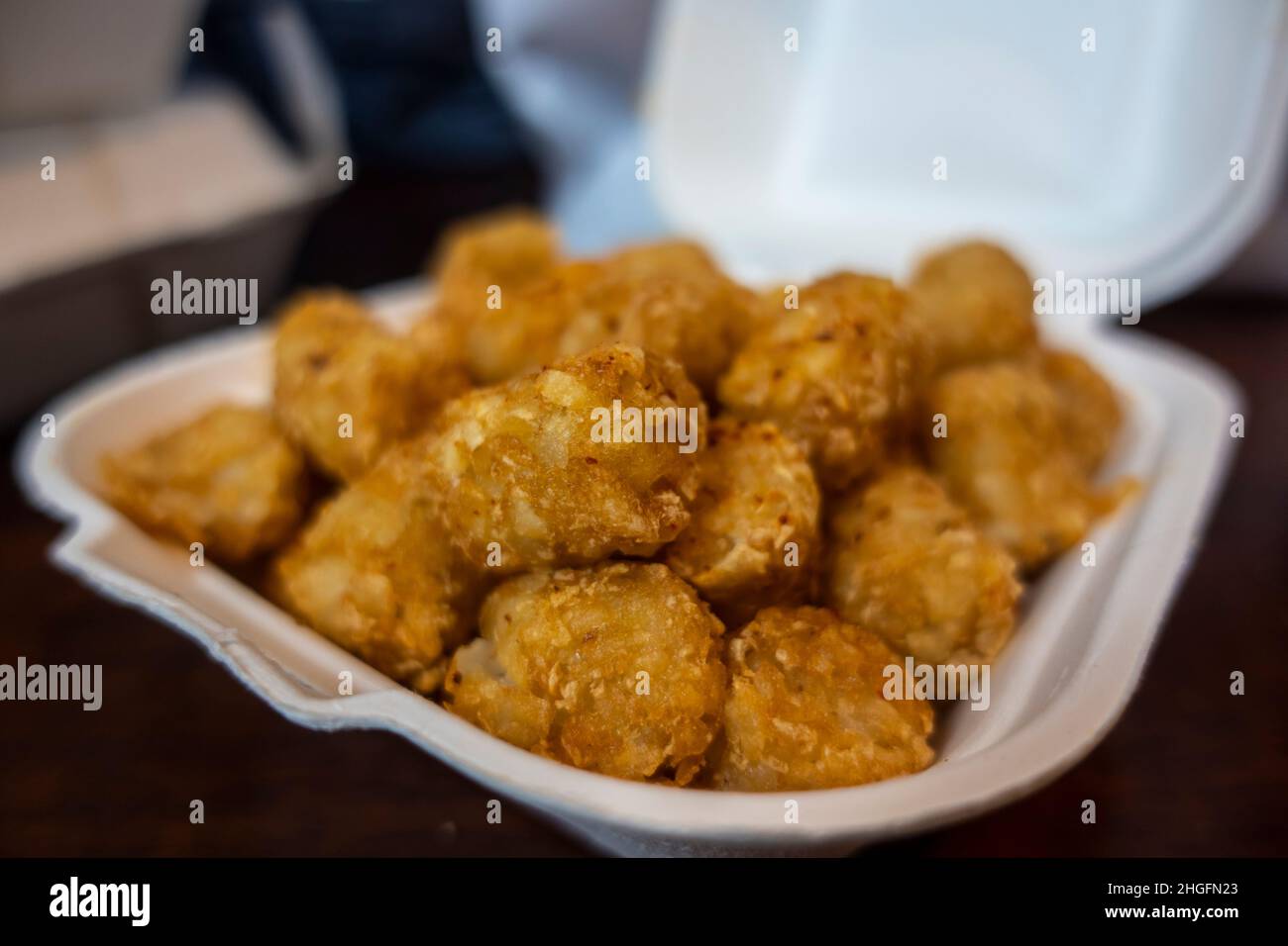 Focalizzazione selettiva di croccanti tatere marroni dorate in un contenitore bianco in polistirolo da andare da un ristorante. Foto Stock