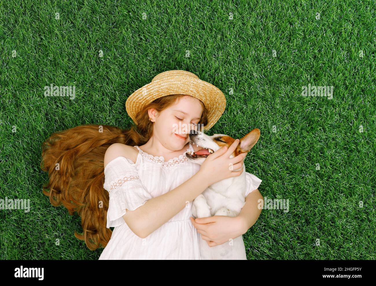 Carina ragazza e cane abbracciare, baciare e sdraiati sul verde erba nel parco primaverile. Primavera, Pasqua, amici concetto. Foto Stock