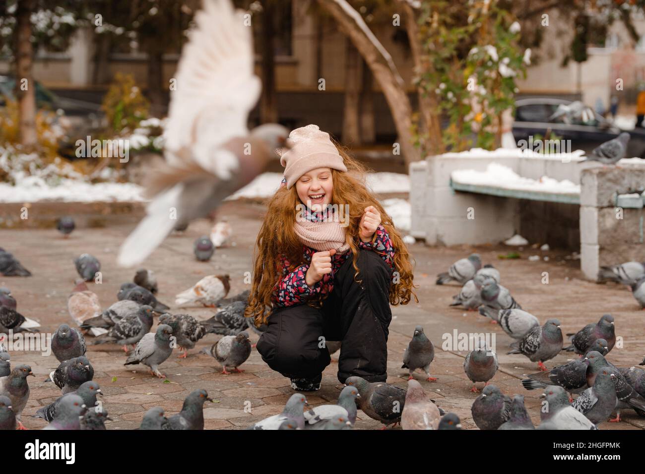 Cute ragazza sta alimentando piccioni con bella giornata invernale all'aperto. Foto Stock