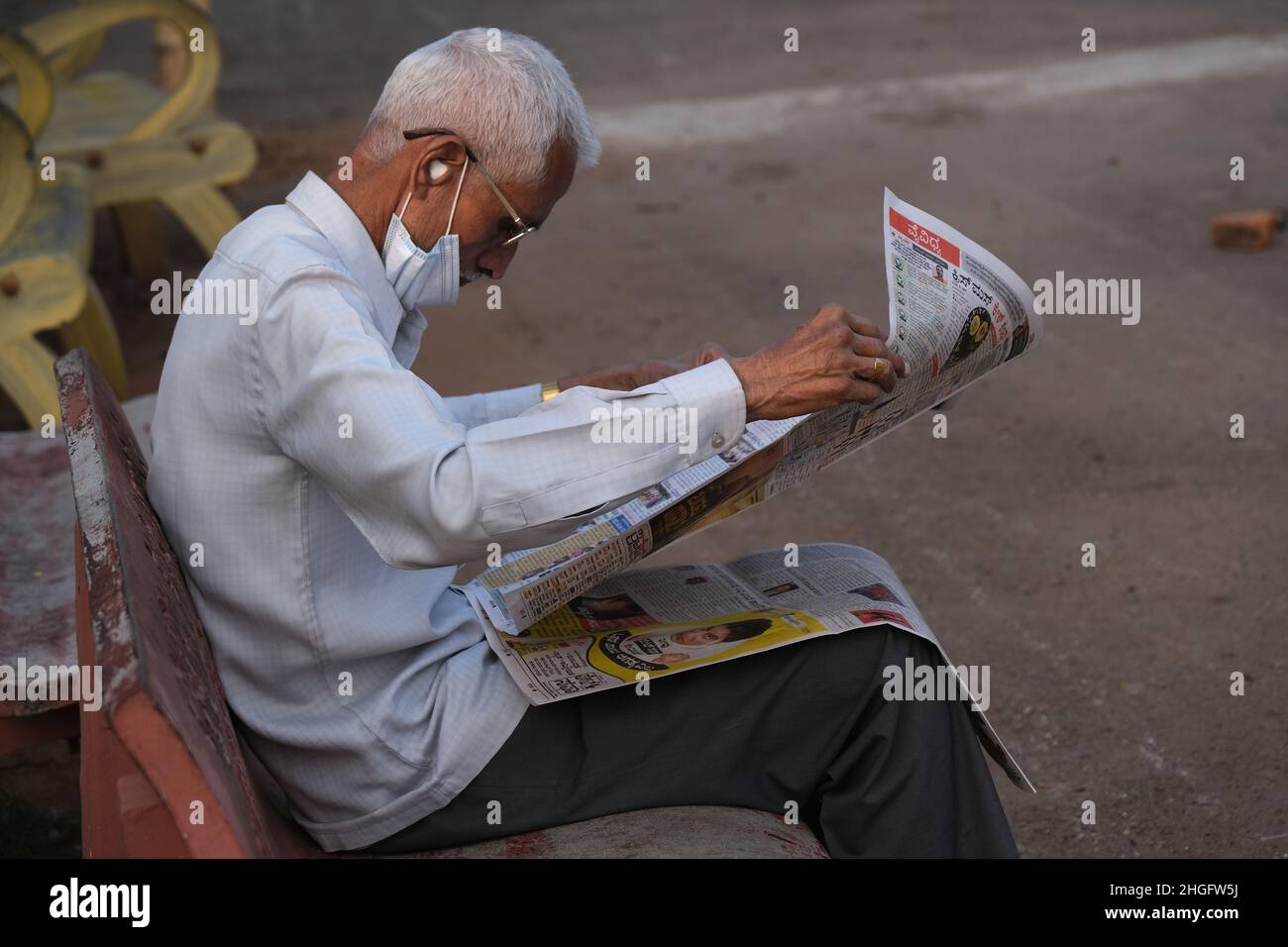 Karnataka, INDIA - 22 dicembre 2021 : Unidentified Man siede e legge comodamente il giornale indiano sulla strada di Udupi. Foto Stock