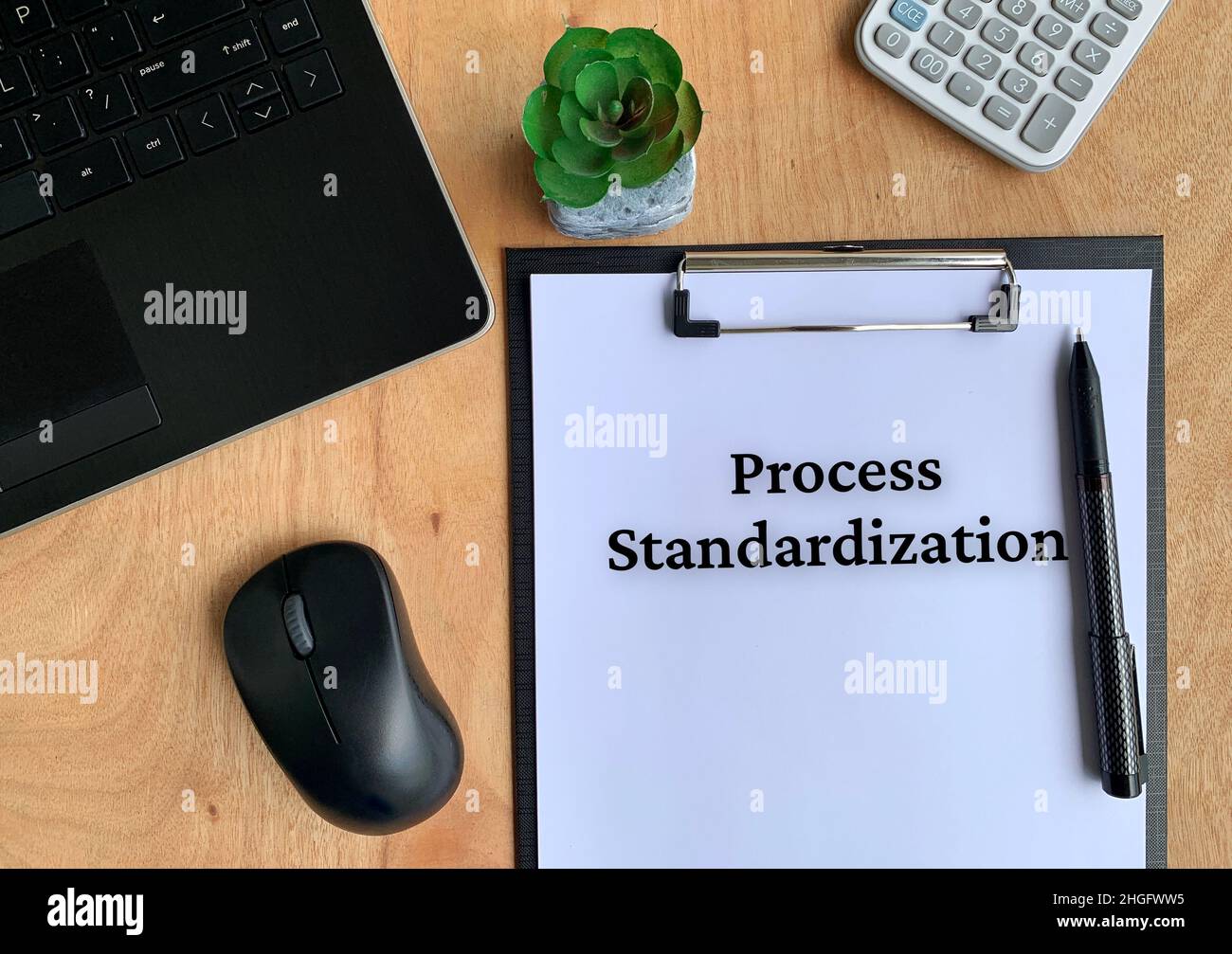 Elaborare il testo di standardizzazione su carta con penna, pianta, mouse, computer portatile, calcolatrice e sfondo marrone tabella. Concetto aziendale. Foto Stock