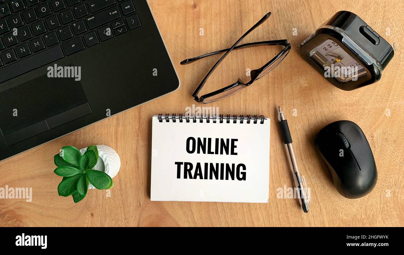 Testo di formazione online su notebook con notebook, penna, mouse, piante, occhiali e sfondo marrone del tavolo. Concetto di business online Foto Stock