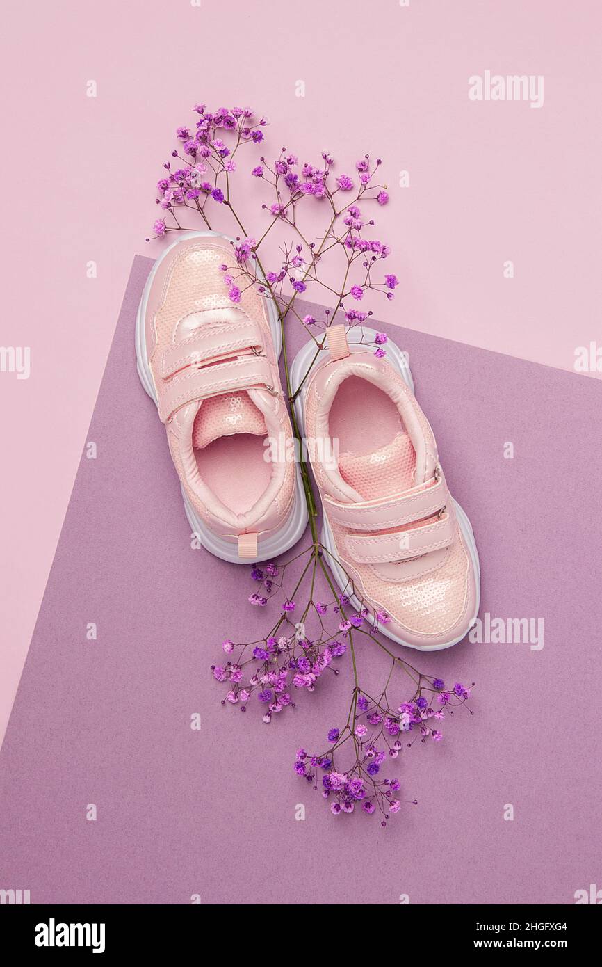 Scarpe sportive, sneakers e fiori naturali su sfondo viola rosa. Concetto di sport primaverile. Vista dall'alto, disposizione piatta. Foto Stock
