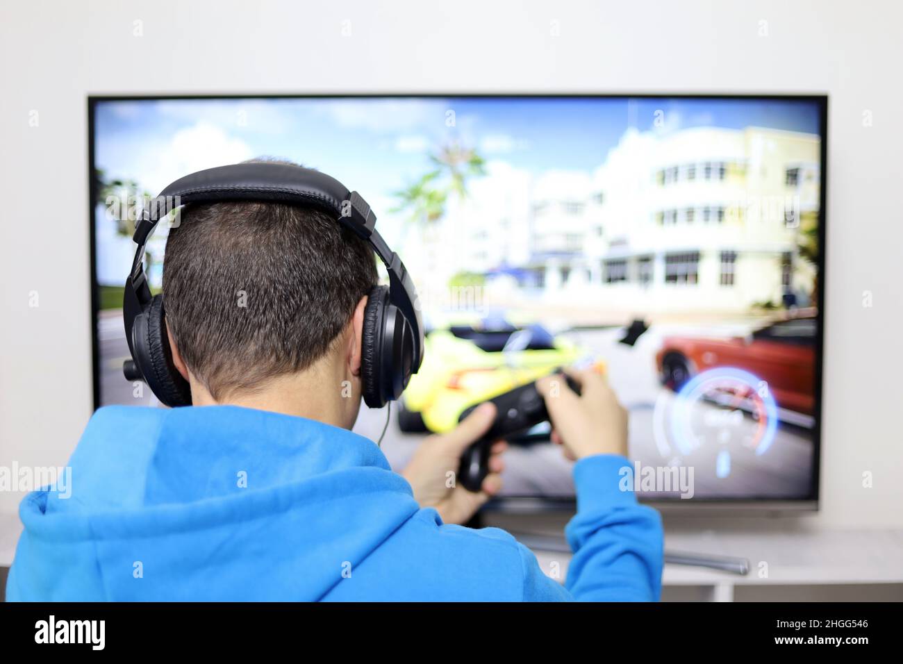 Guy in cuffie giocare con un gamepad un gioco di corse video sullo schermo della TV. Concetto di dipendenza da gioco, tempo libero a casa Foto Stock