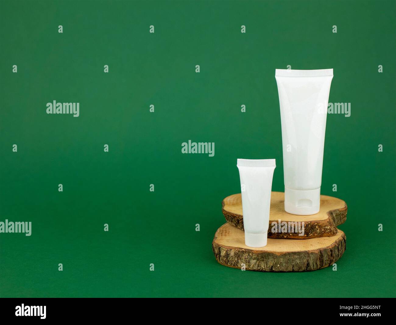 Grandi e piccoli tubi bianchi con crema facciale o mano sulle sezioni trasversali di un albero su sfondo verde, spazio di copia. Concetto di cosmetica naturale, org Foto Stock