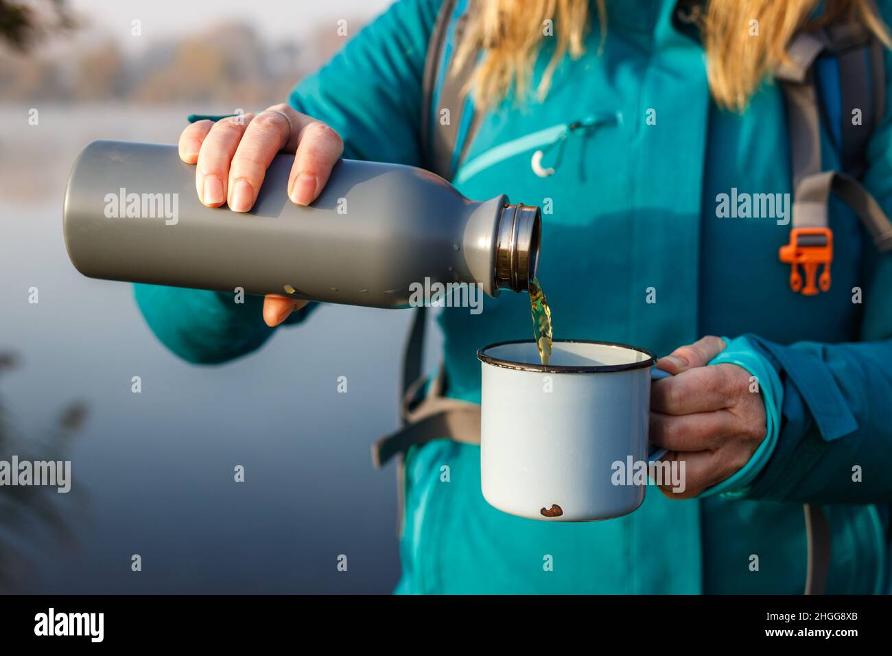 La donna versa la bevanda calda dai thermos nella tazza di corsa. Rinfresco durante le escursioni al lago in tempo freddo Foto Stock