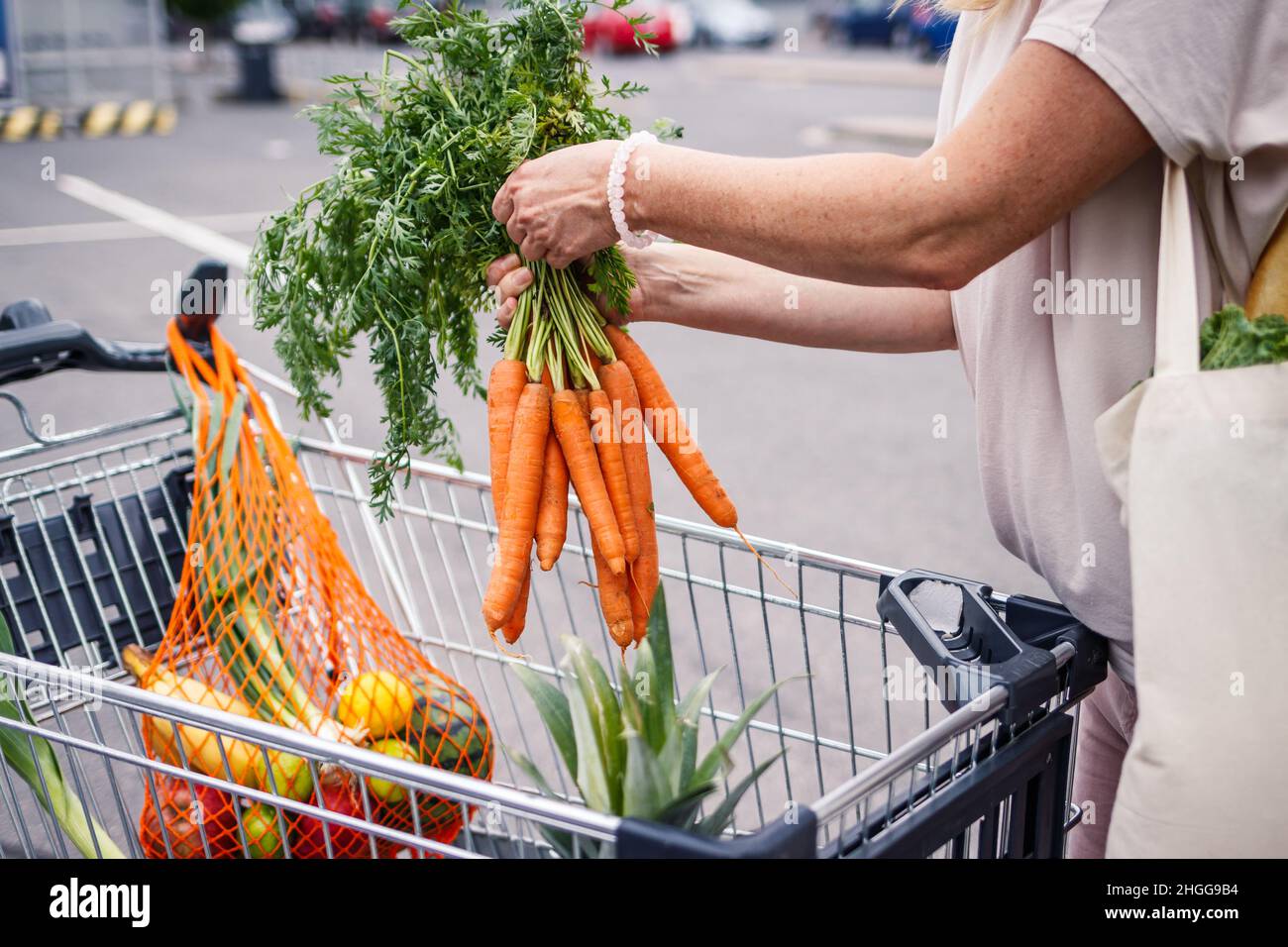 Shopping gratuito di plastica. Donna che raccoglie mazzo di carote dal parcheggio dei cartoni dello shopping. Sacchetto a rete riutilizzabile. Concetto di zero rifiuti Foto Stock
