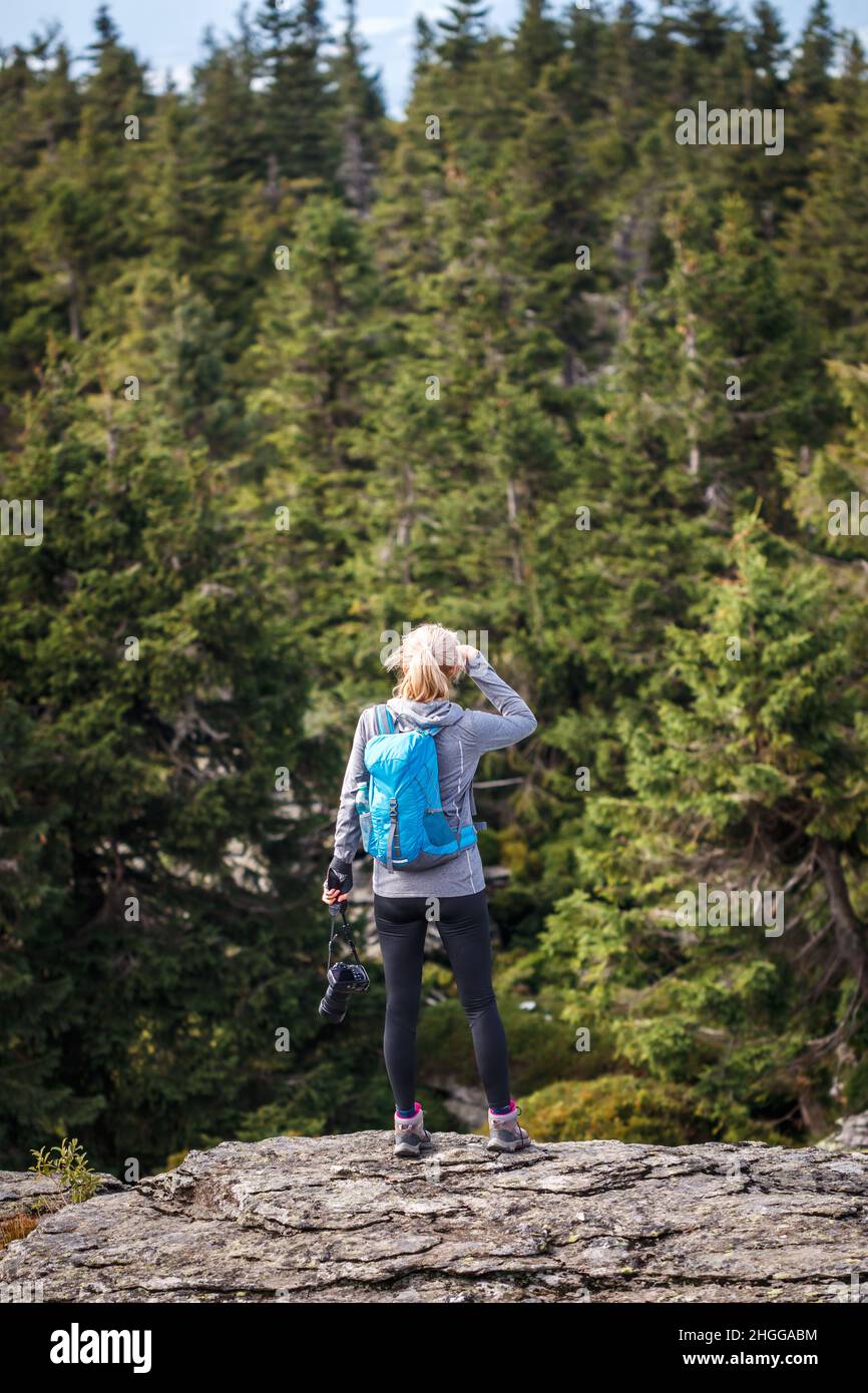 Donna escursionista con macchina fotografica in piedi sul picco roccioso della montagna. Escursioni nella foresta. Stile di vita attivo all'aperto Foto Stock