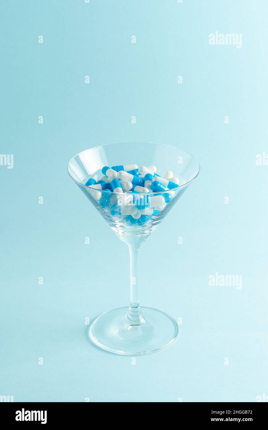 Bicchiere Martini pieno di pillole colorate su sfondo blu. Composizione creativa. Foto Stock