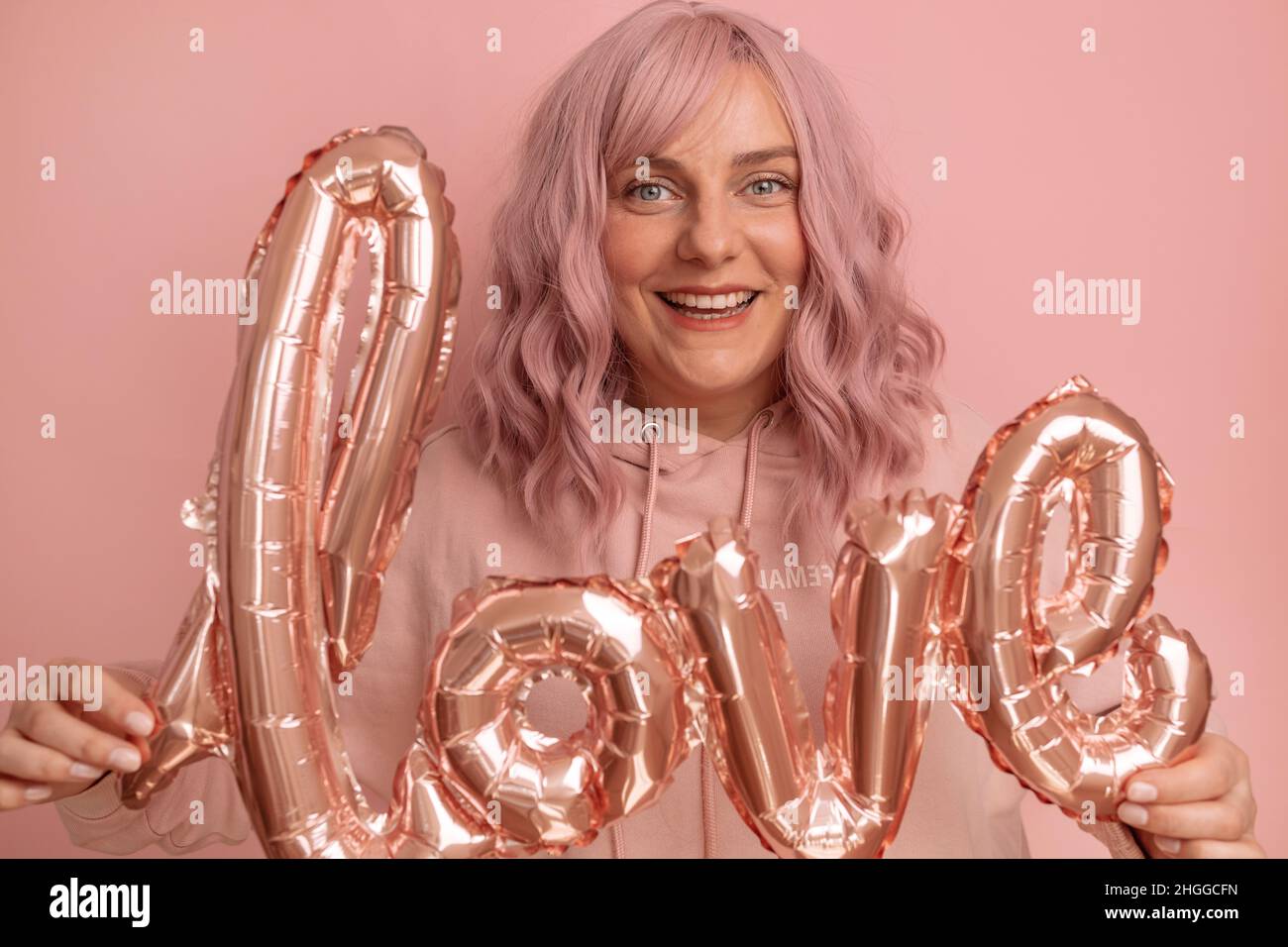 San Valentino banner con bella giovane 20s donna celebrazione che ha divertente tenere foglio di amore parola palloncini su sfondo rosa. Festa della mamma, compleanno Foto Stock