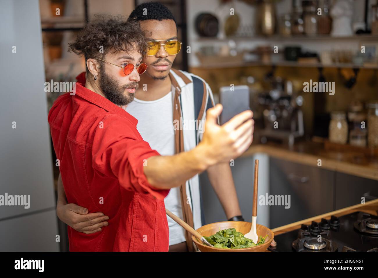 Due eleganti ragazzi dal vestito brillante che prendono selfie al telefono al chiuso Foto Stock