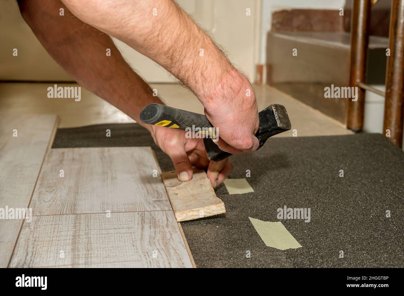 Martello tenuto da una mano di una persona con le dita amputate come egli lavora posa pavimenti in casa sua. Foto Stock