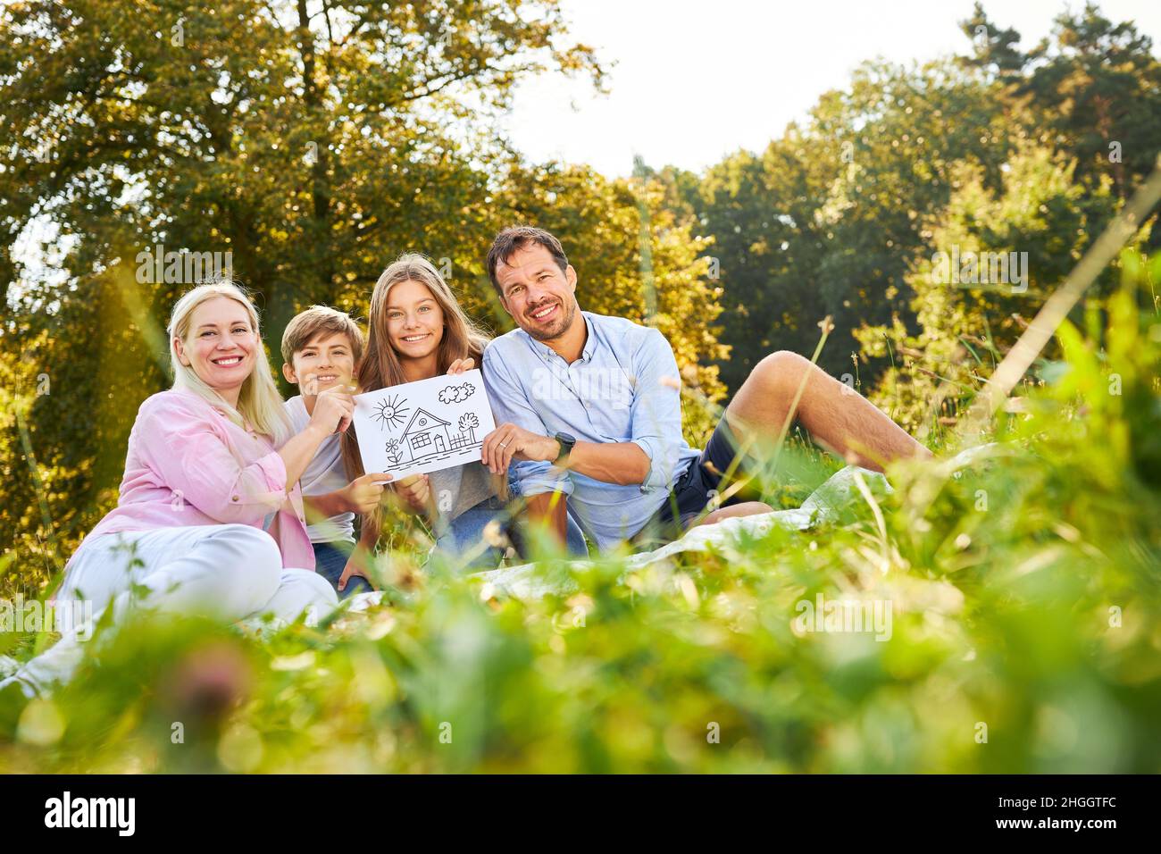 Famiglia felice seduta su un prato verde con disegno della propria casa come un futuro Foto Stock