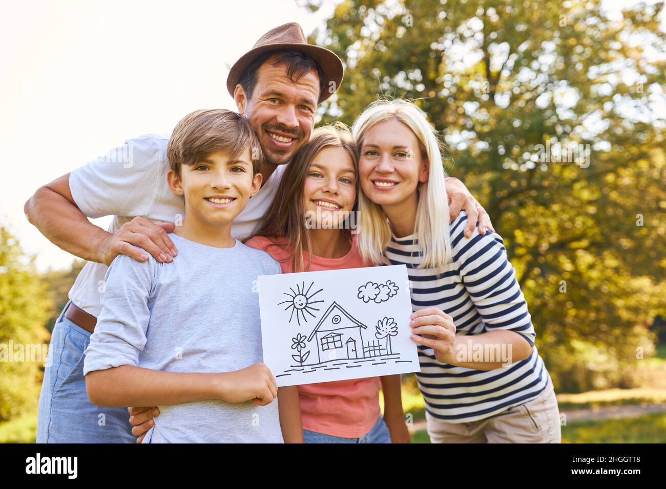 Famiglia felice con due bambini che tengono disegno che simboleggia la costruzione della casa e la proprietà della casa Foto Stock