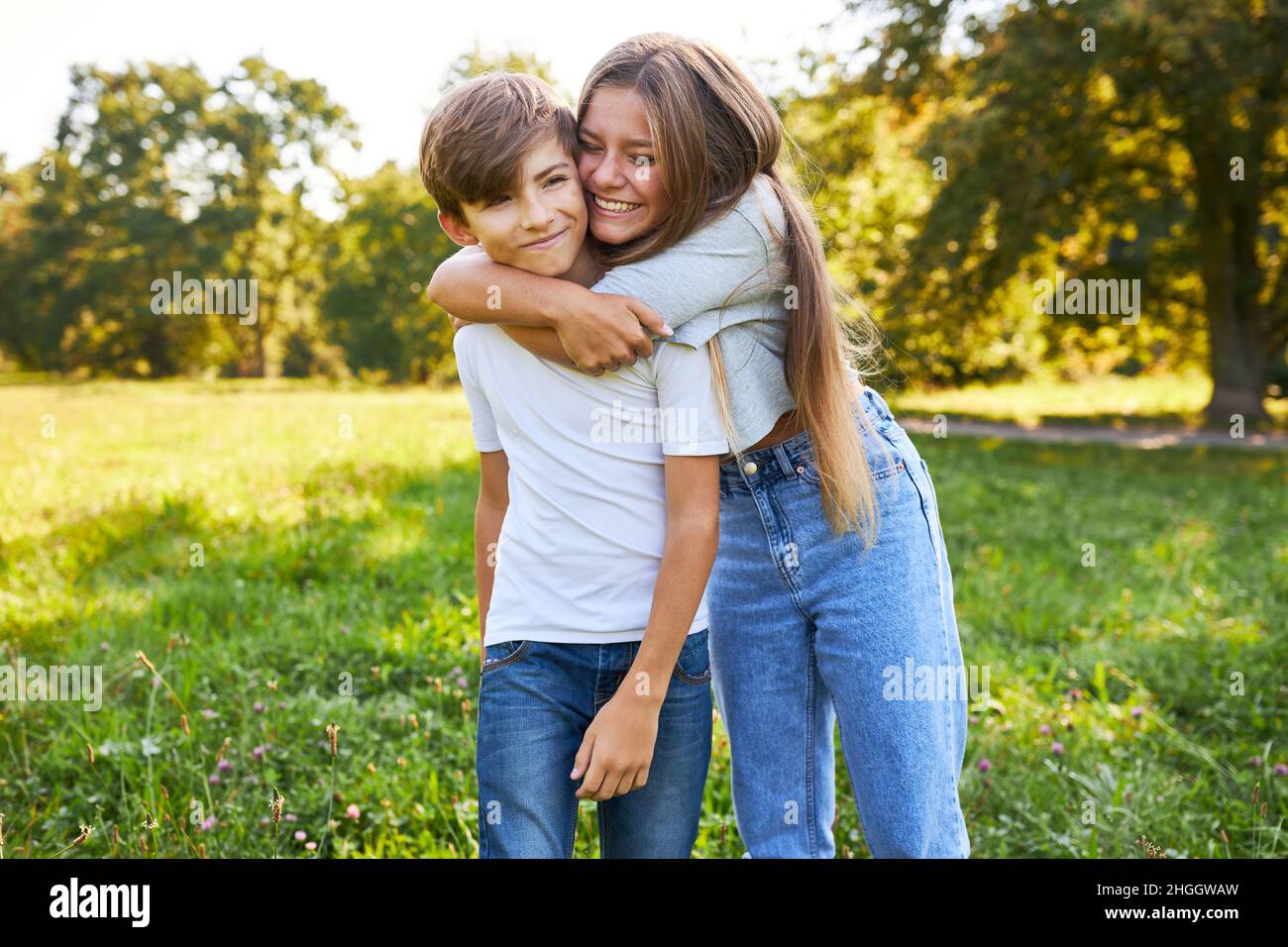 Sorella abbraccia felicemente il suo fratellino su un prato in natura Foto Stock