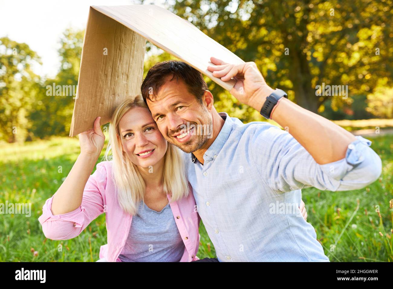 Felice giovane coppia in parco con tetto sopra la testa simboleggia la proprietà e la sicurezza della casa Foto Stock