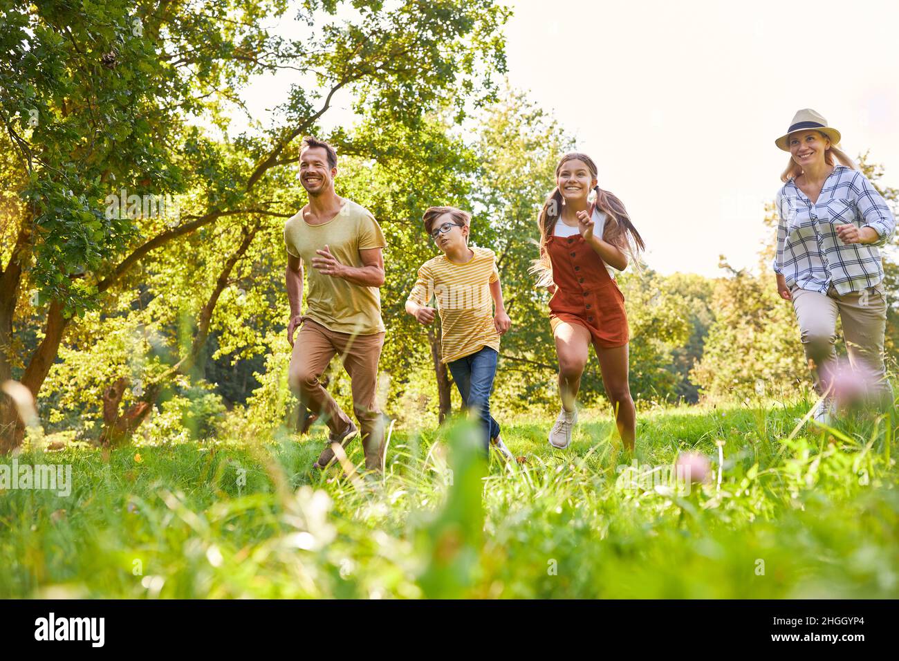 Famiglia felice con due bambini che corrono attraverso un prato in natura Foto Stock