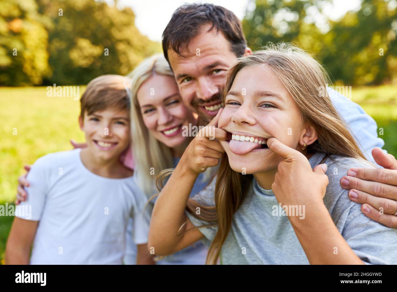 Ragazza felice che si volava intorno mostrando la lingua con i genitori e fratello in estate Foto Stock